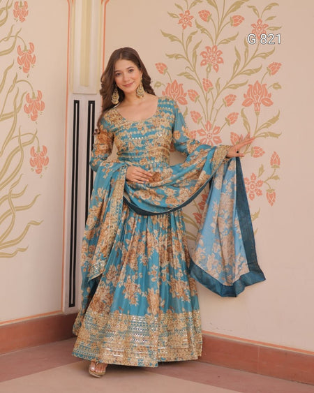 Woman in a blue and gold traditional outfit standing against a decorative wall.