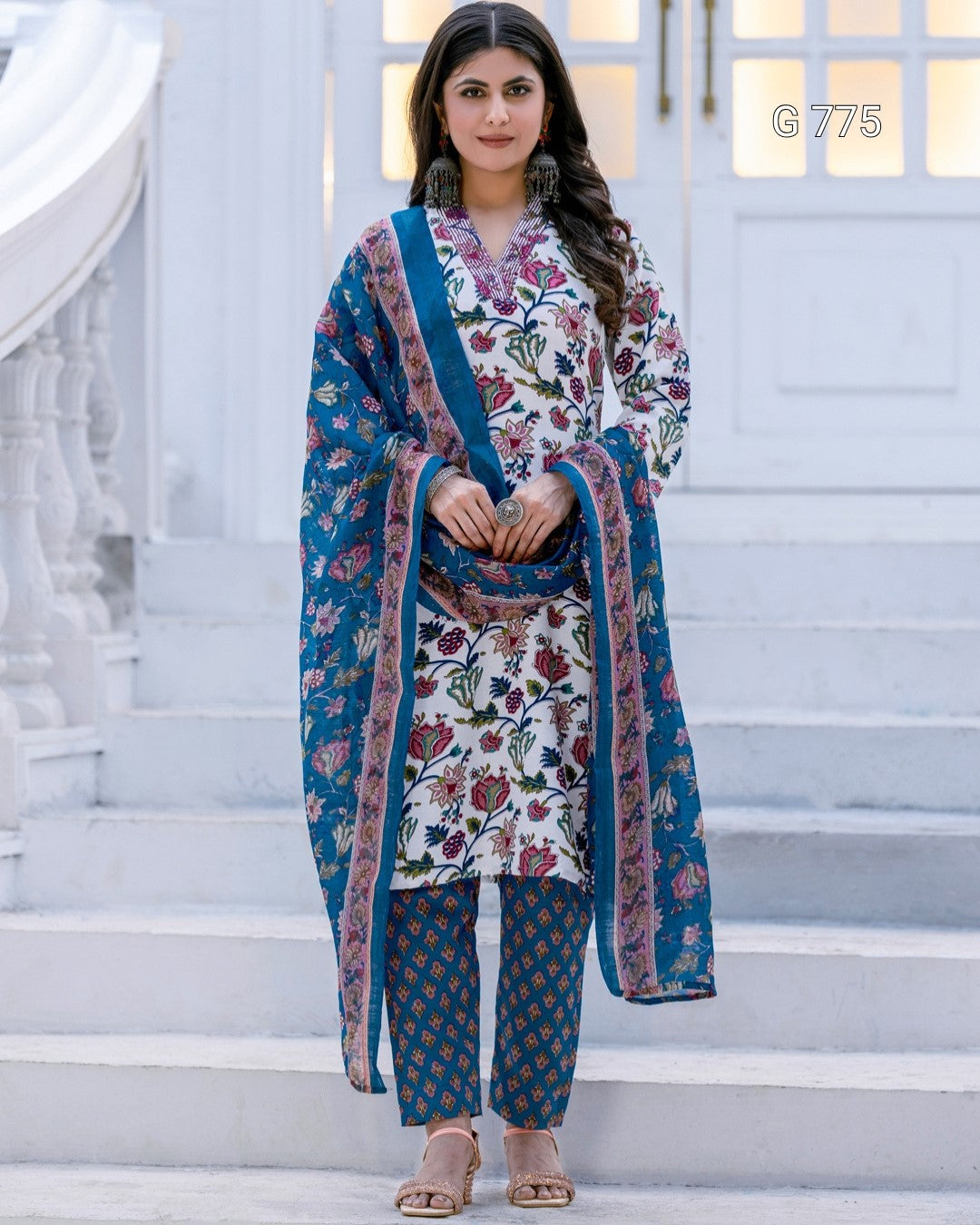 Woman in traditional outfit with floral patterns standing on white steps.