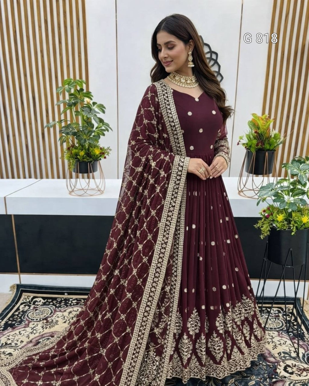Woman in a maroon traditional outfit with gold embroidery in a decorated room.