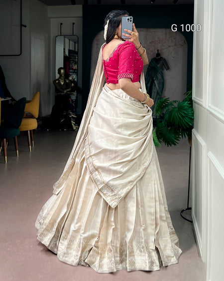 A woman takes a mirror selfie in a boutique wearing a traditional Indian saree. The saree consists of a voluminous cream-colored skirt with a subtle sheen and border, paired with a bright pink embroidered blouse.