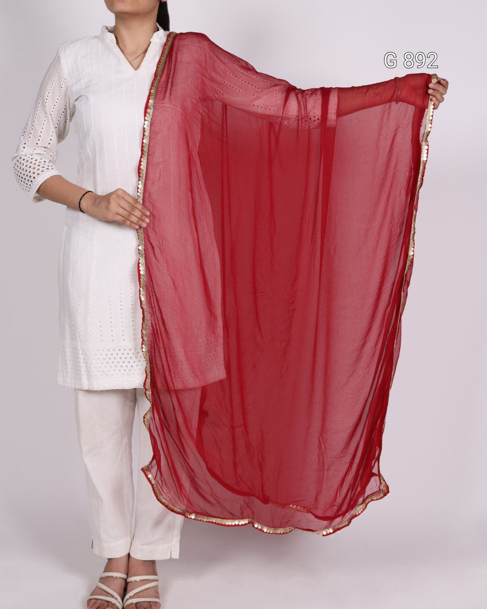 Person wearing a white outfit with a red dupatta on a plain background