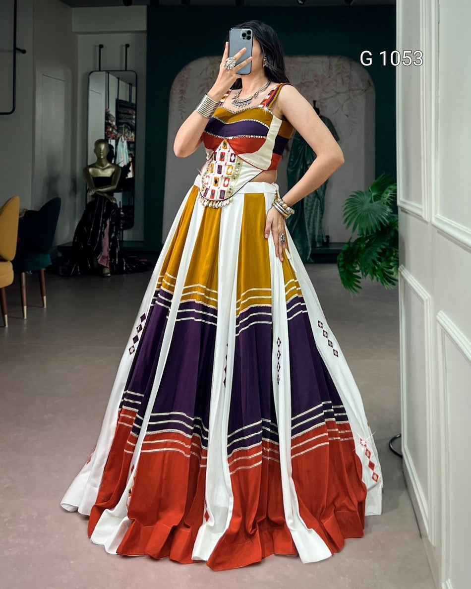A woman takes a mirror selfie wearing a long, sleeveless, high-waisted maxi dress with a multicolor block-print pattern in mustard yellow, purple, orange, and white. The dress features a fitted bodice with a geometric pattern and a voluminous skirt.
