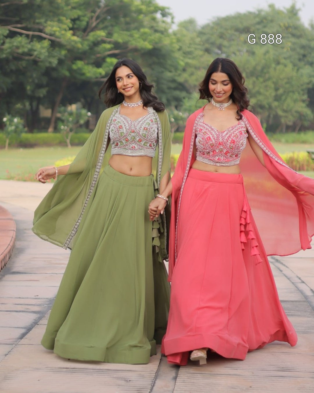 Two women in traditional green and pink lehengas standing outdoors with trees in the background.