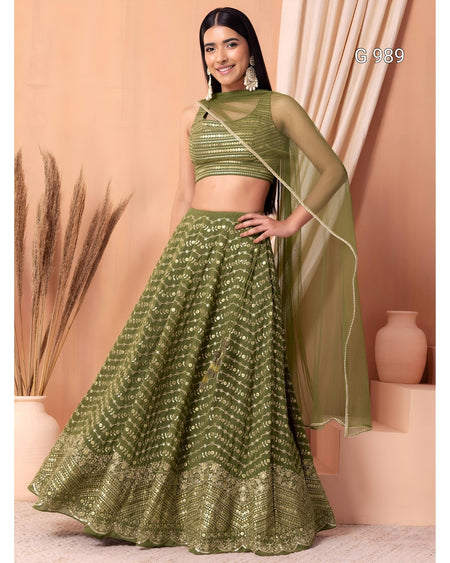 A woman models an olive green lehenga choli set with a matching dupatta. The set features a sleeveless crop top with horizontal metallic embroidery, a full flared skirt with vertical metallic embroidery, and a sheer long-sleeve dupatta.