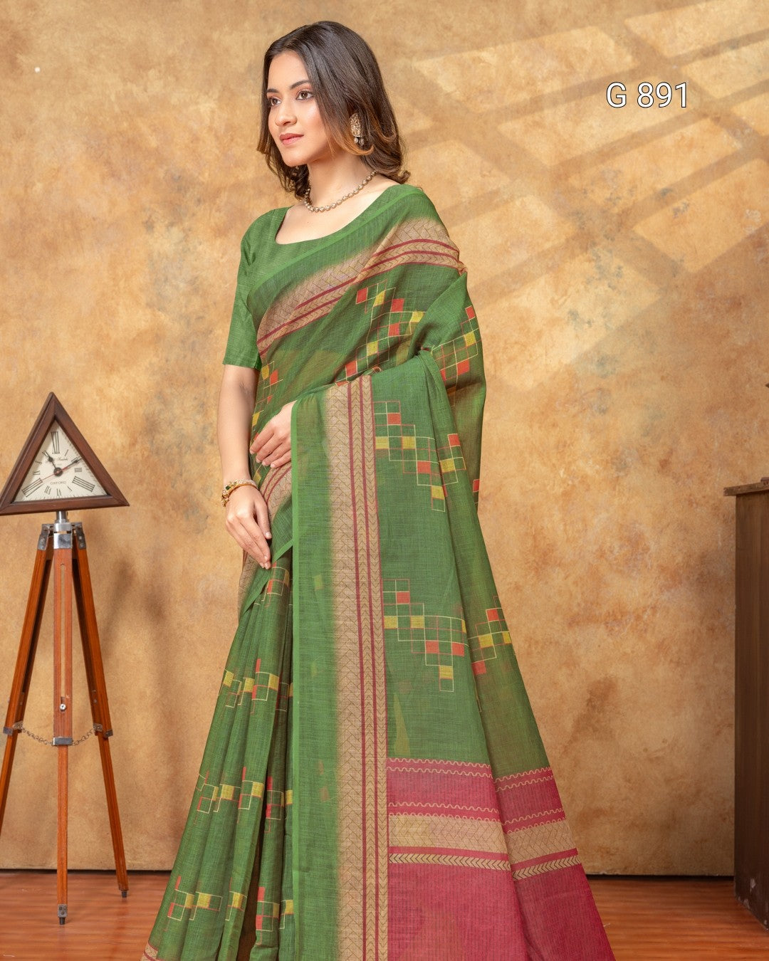 Woman wearing a green saree with a patterned border against a brown background