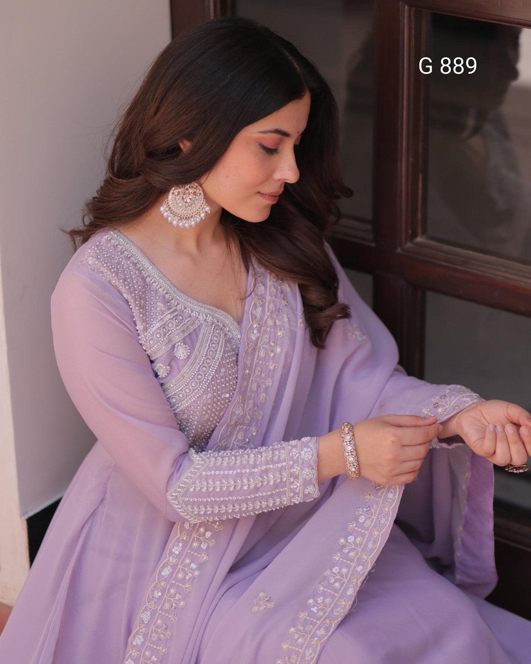 Woman in a lavender traditional outfit with intricate designs, sitting indoors.