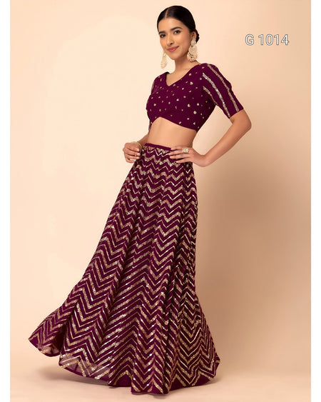 A woman modeling a deep purple lehenga choli set with silver zari chevron patterns, set against a solid beige background.