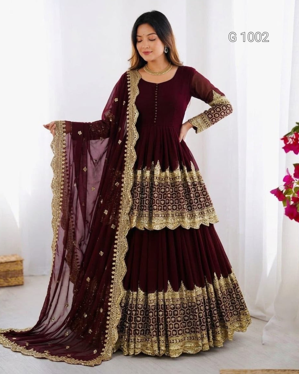 A woman models a deep maroon Anarkali gown with gold embroidery and a matching sheer dupatta, set against a white curtain background.