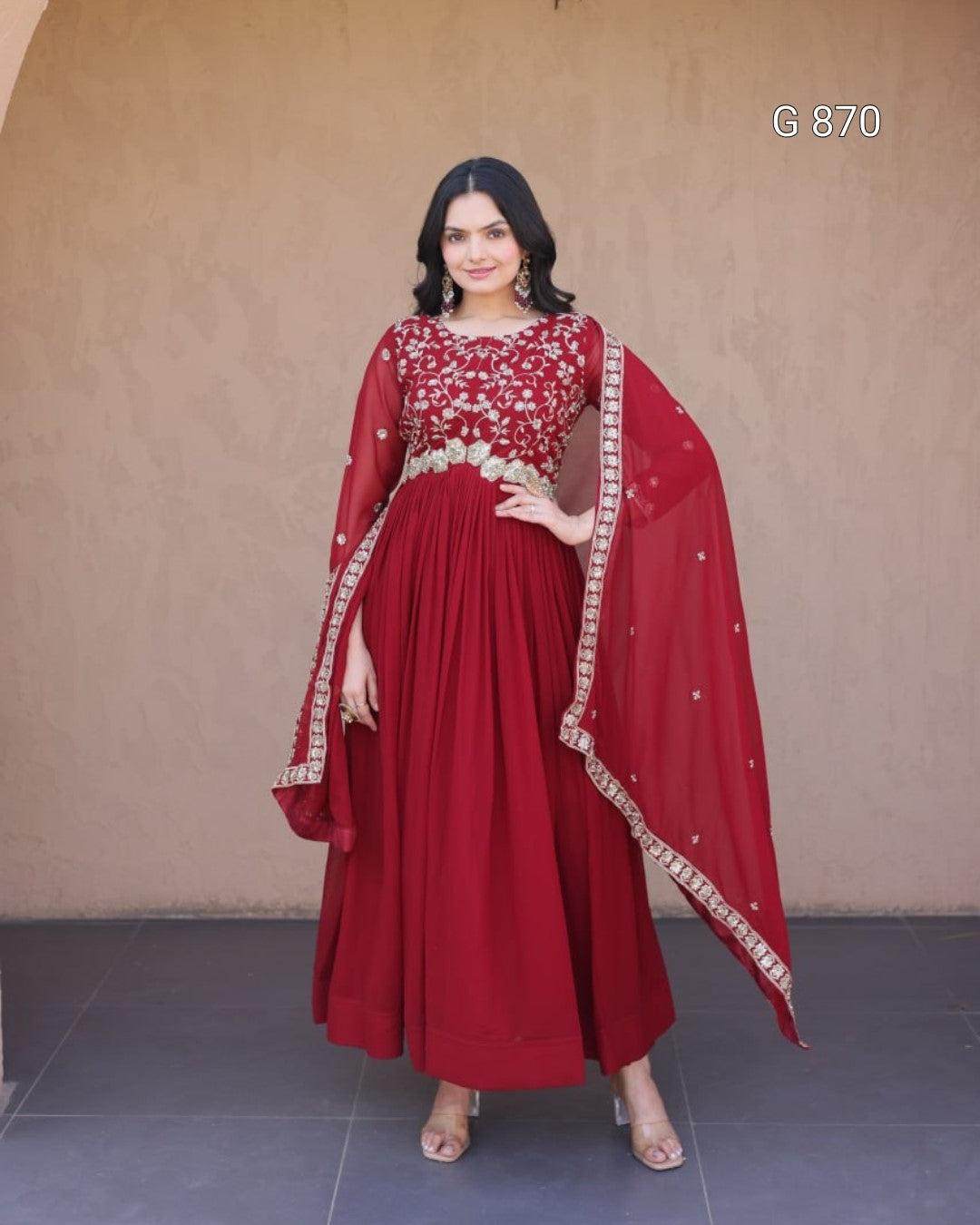 Woman wearing a red traditional outfit with a matching dupatta against a plain background