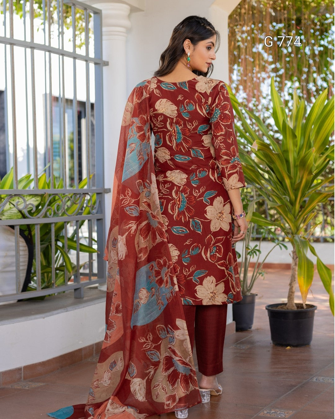 Woman wearing a floral outfit standing on a balcony with plants in the background