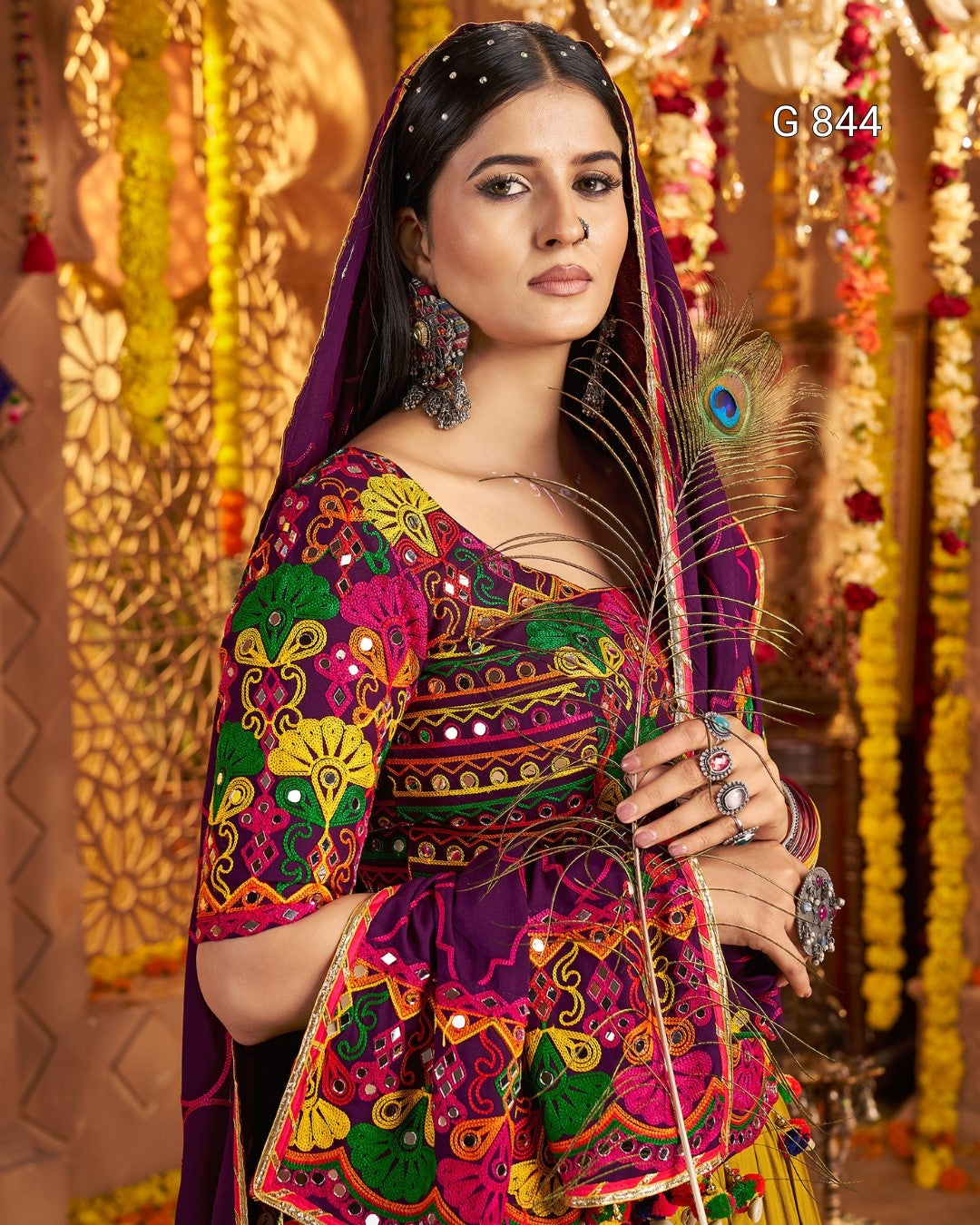 Woman in a colorful traditional outfit holding a peacock feather, with decorative background