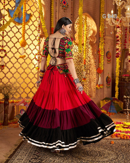 Woman in a colorful traditional outfit with a red and black skirt in a decorated indoor setting.