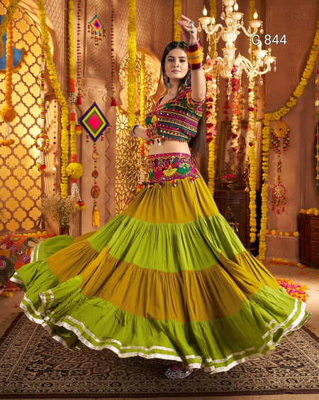 Woman in traditional colorful outfit with a vibrant green and yellow skirt, standing in an ornate decorated room.