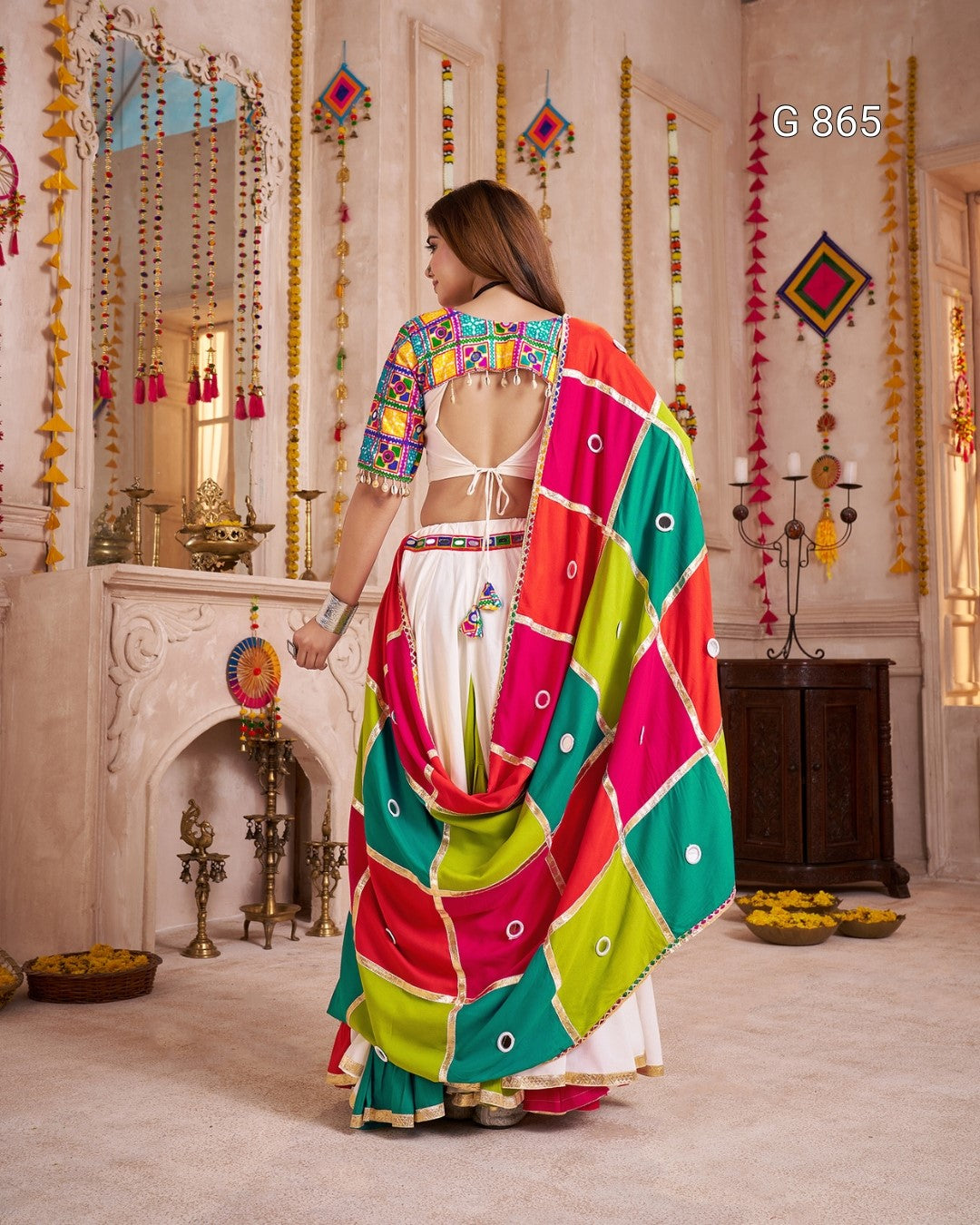Woman in a colorful saree standing in a decorated room with traditional decor.