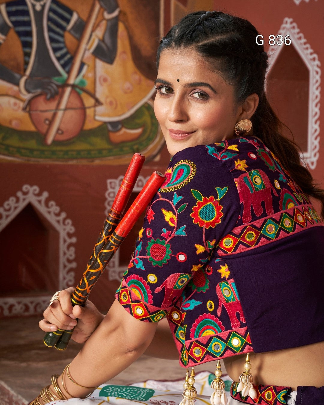Woman in traditional attire holding red sticks with a colorful background