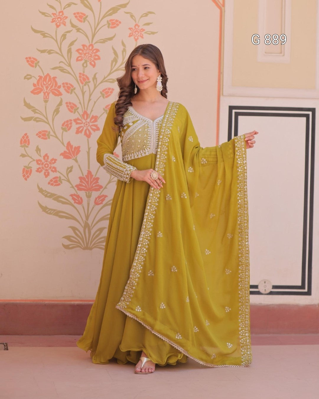 Woman in a green traditional outfit with floral patterns in a decorated room.