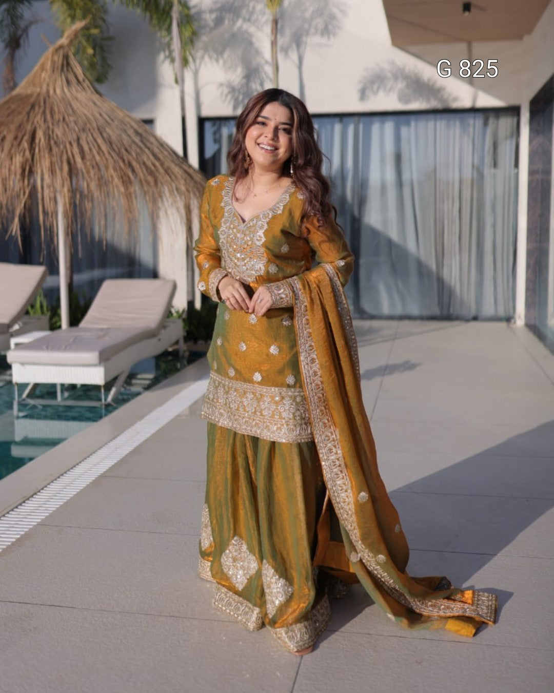 Woman in a traditional mustard yellow outfit standing by a poolside.