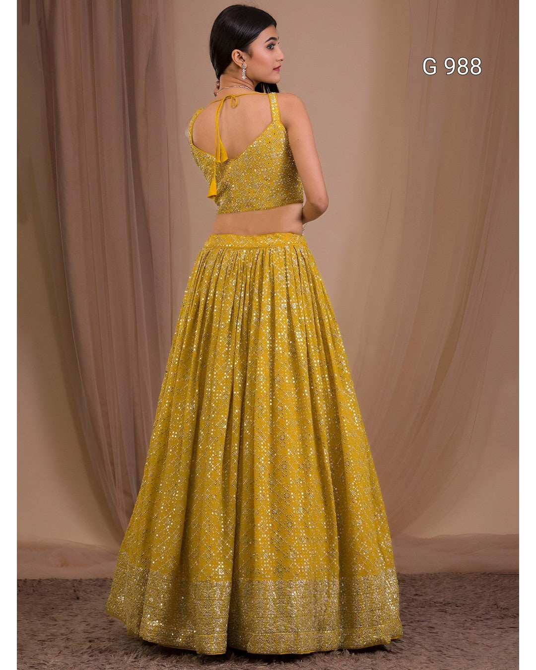 A woman modeling a yellow embroidered traditional outfit with a sleeveless fitted top and a full flared skirt, photographed against a draped beige backdrop. The text 'G 988' appears in the upper right.