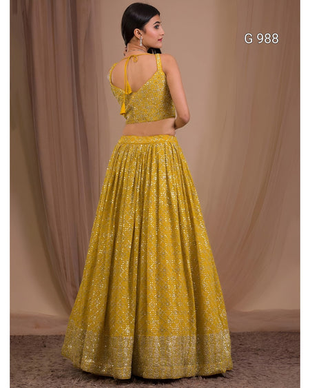 A woman modeling a yellow embroidered traditional outfit with a sleeveless fitted top and a full flared skirt, photographed against a draped beige backdrop. The text 'G 988' appears in the upper right.