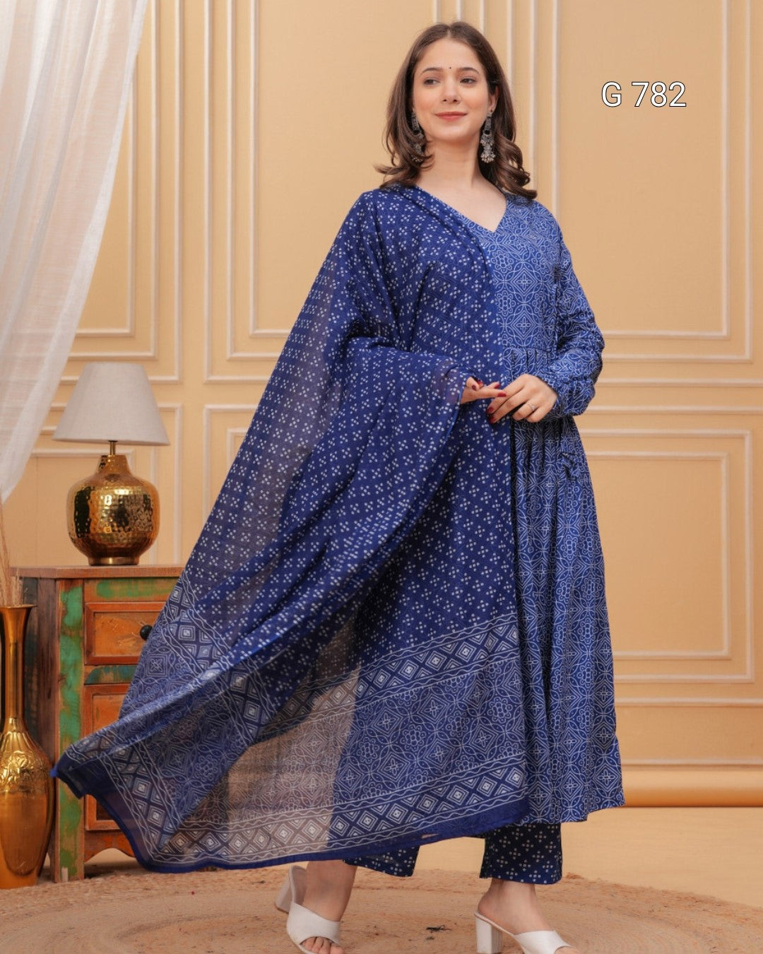 Woman wearing a blue patterned dress in a room with beige walls and decorative elements.