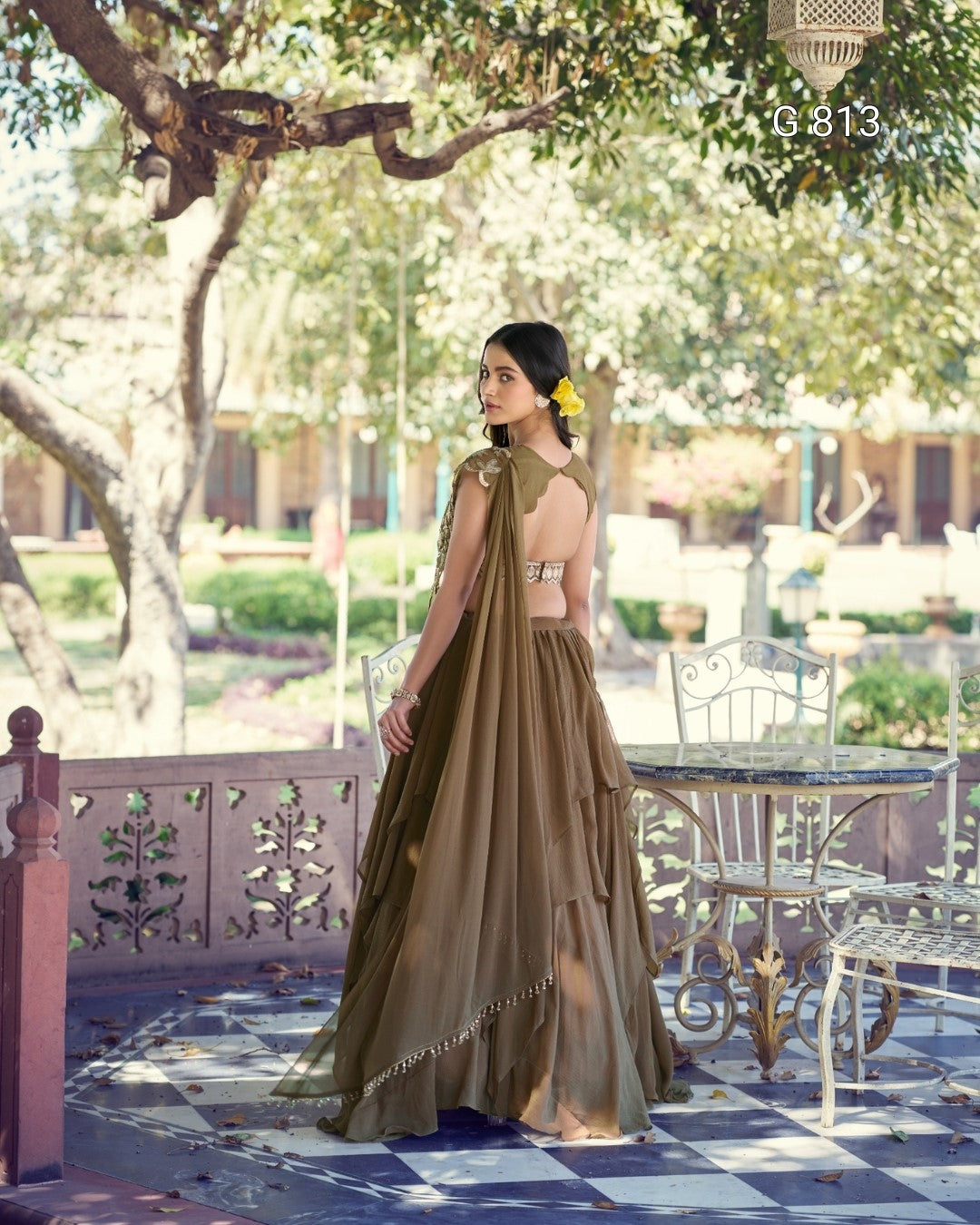 Woman in a long, flowing dress standing in a garden setting with trees and a table in the background.