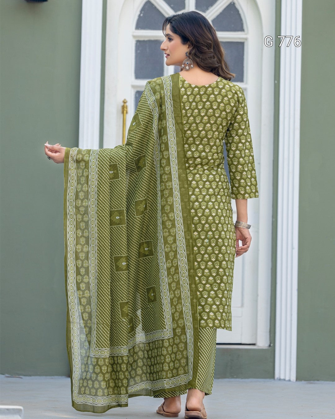 Woman wearing a green traditional outfit with a matching dupatta in front of a white door.
