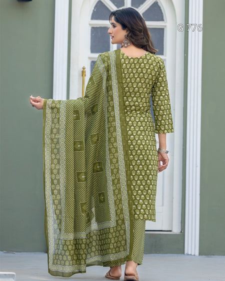 Woman wearing a green traditional outfit with a matching dupatta in front of a white door.