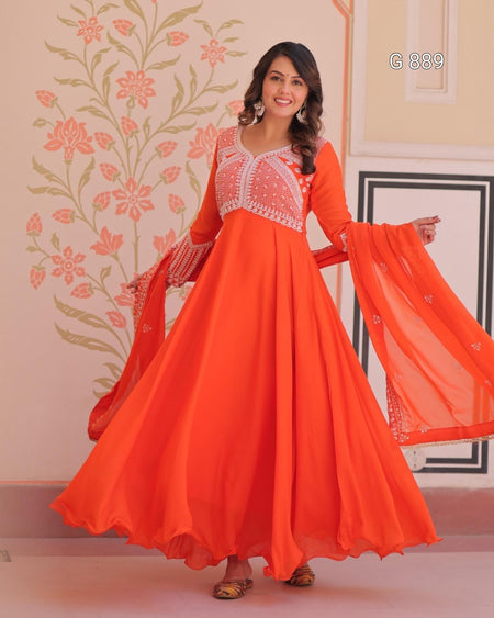 Woman wearing an orange traditional outfit with white embroidery in a decorated room.