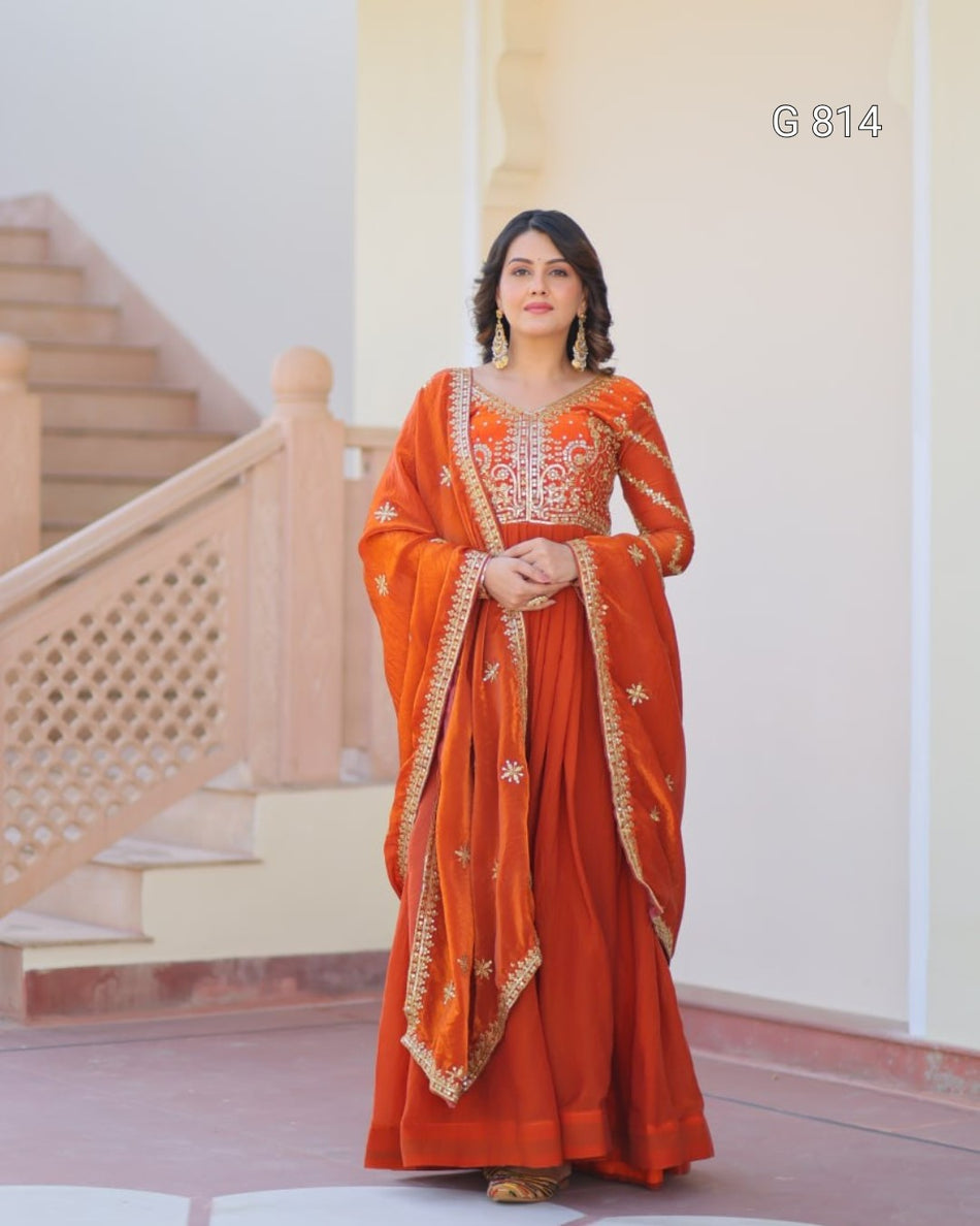 Woman in an orange saree with gold embroidery standing in a well-lit room.