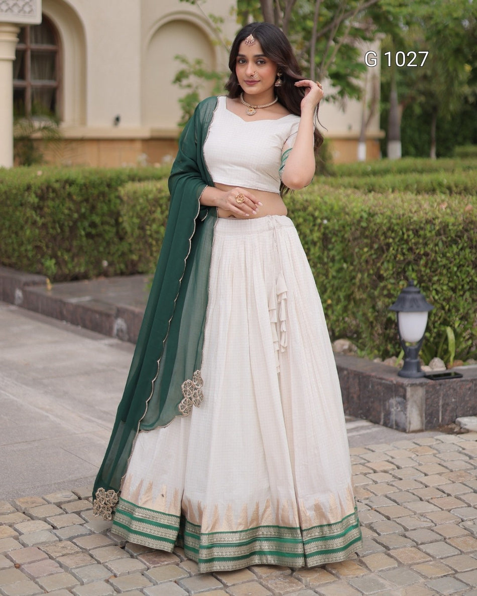A woman models a traditional Indian outfit consisting of a white sleeveless kurta, a matching flared skirt, and a dark green dupatta with gold borders, set against an outdoor garden background.