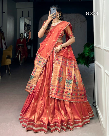 Woman wearing a traditional orange saree with intricate patterns indoors.