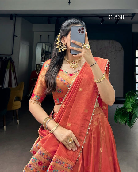 Woman in an orange saree with jewelry taking a mirror selfie.