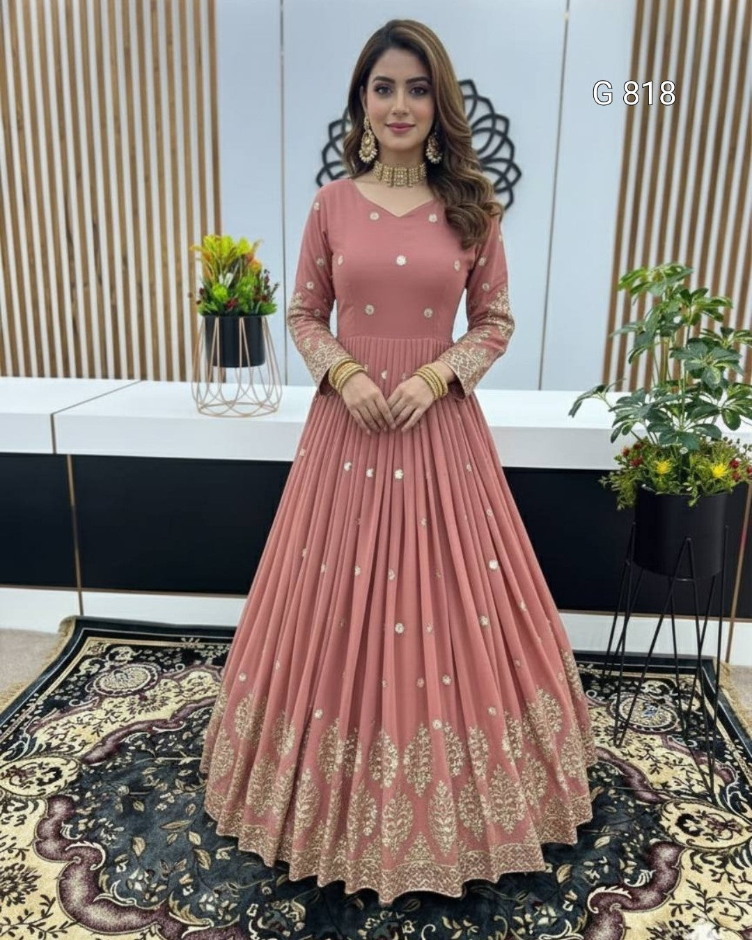 Woman wearing a pink anarkali suit with gold embroidery in an indoor setting.