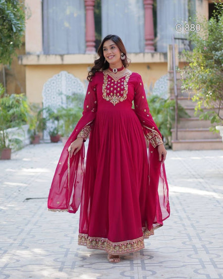 Woman in a red traditional outfit with gold embroidery standing outdoors.