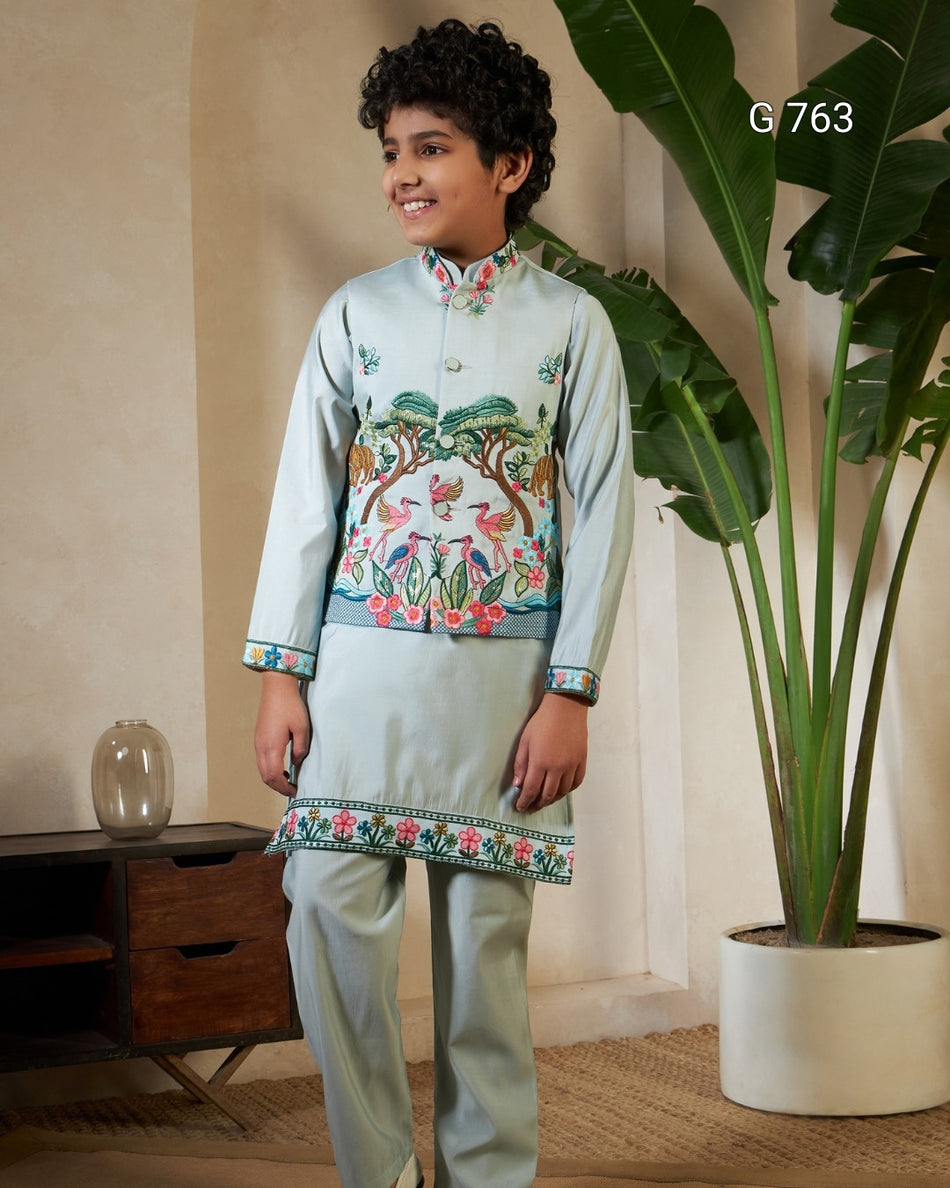 Young boy in traditional embroidered outfit standing indoors with a plant in the background
