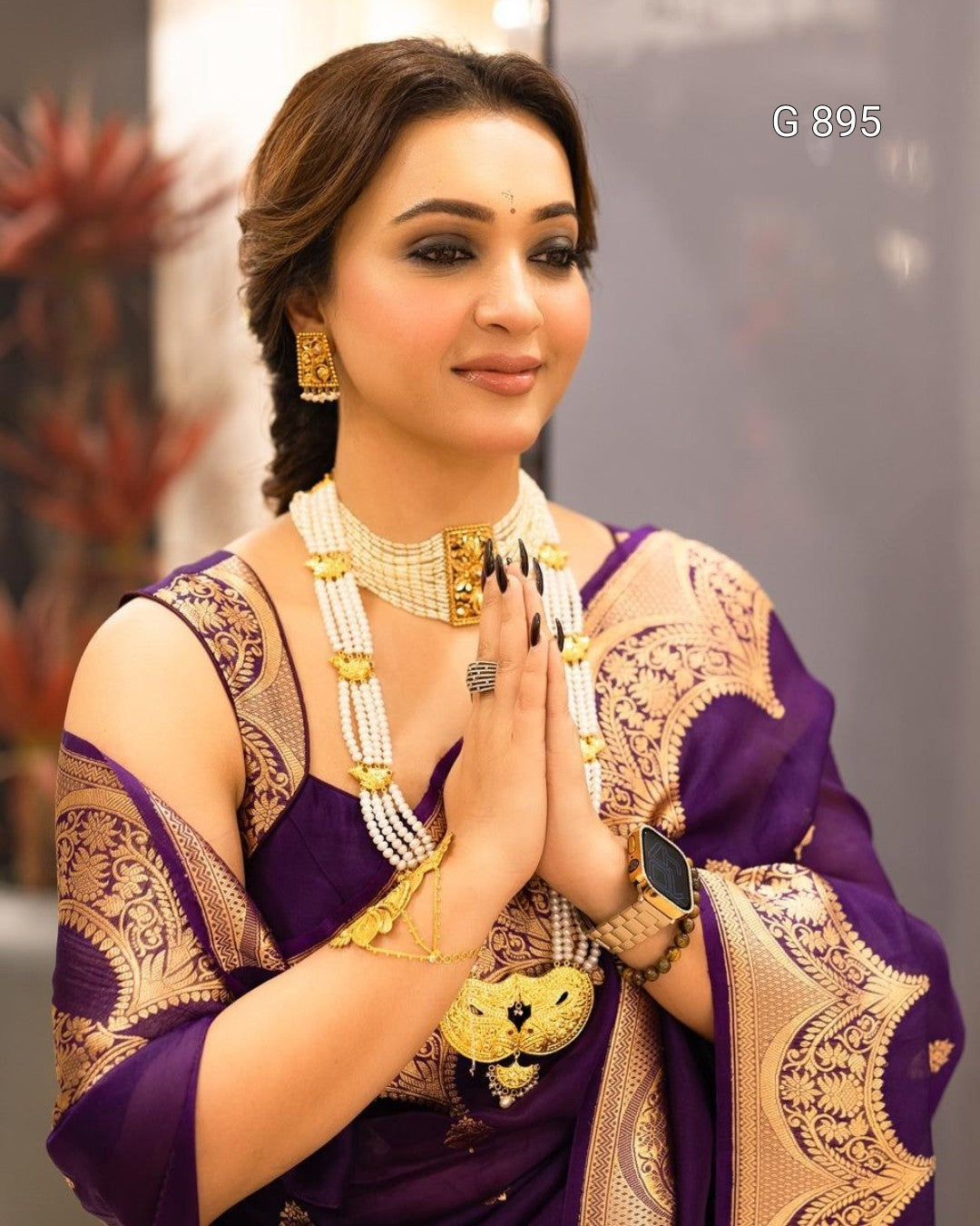 Woman in traditional attire with gold jewelry, posing indoors.