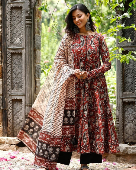Woman wearing a patterned traditional outfit standing in a garden setting.
