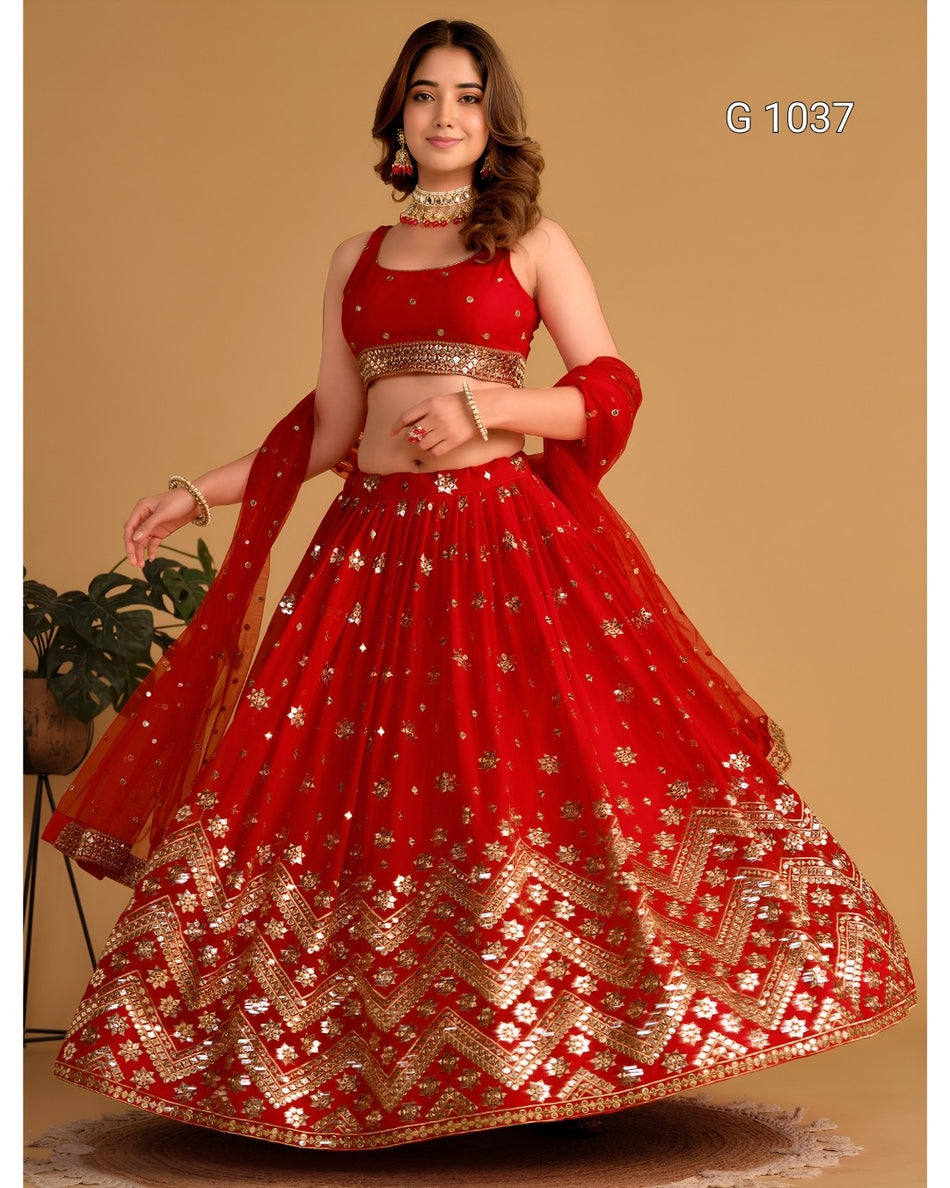 A woman modeling a red and gold embroidered Indian lehenga choli set against a solid beige background. The set features a red sleeveless blouse with gold embroidery, a matching flared skirt with intricate gold patterns, and a red dupatta draped over her shoulder.