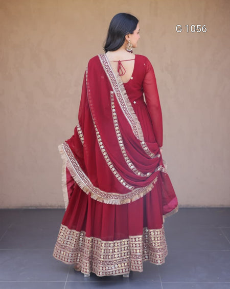 A woman wearing a deep red traditional ethnic outfit with gold embroidered borders, shown from the back against a plain beige wall.