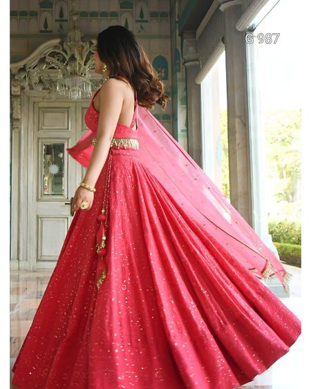 A woman wearing a bright pink lehenga choli with gold embellishments and a matching dupatta, photographed indoors near large windows.
