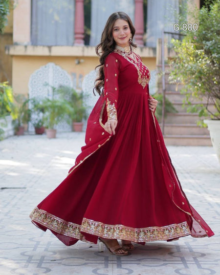 Woman in a red traditional outfit with gold embroidery standing outdoors.