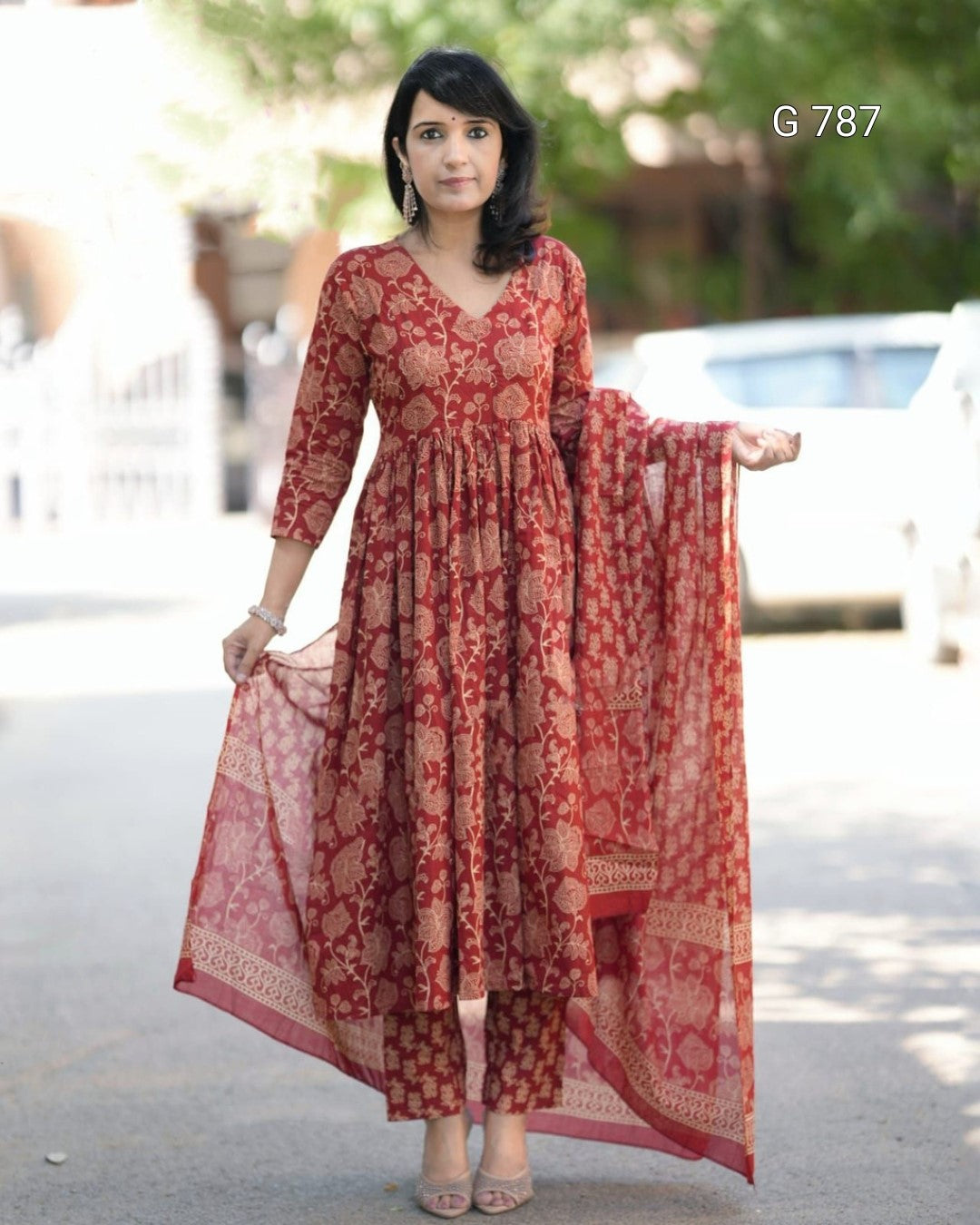 Woman wearing a red patterned dress with a matching dupatta outdoors.