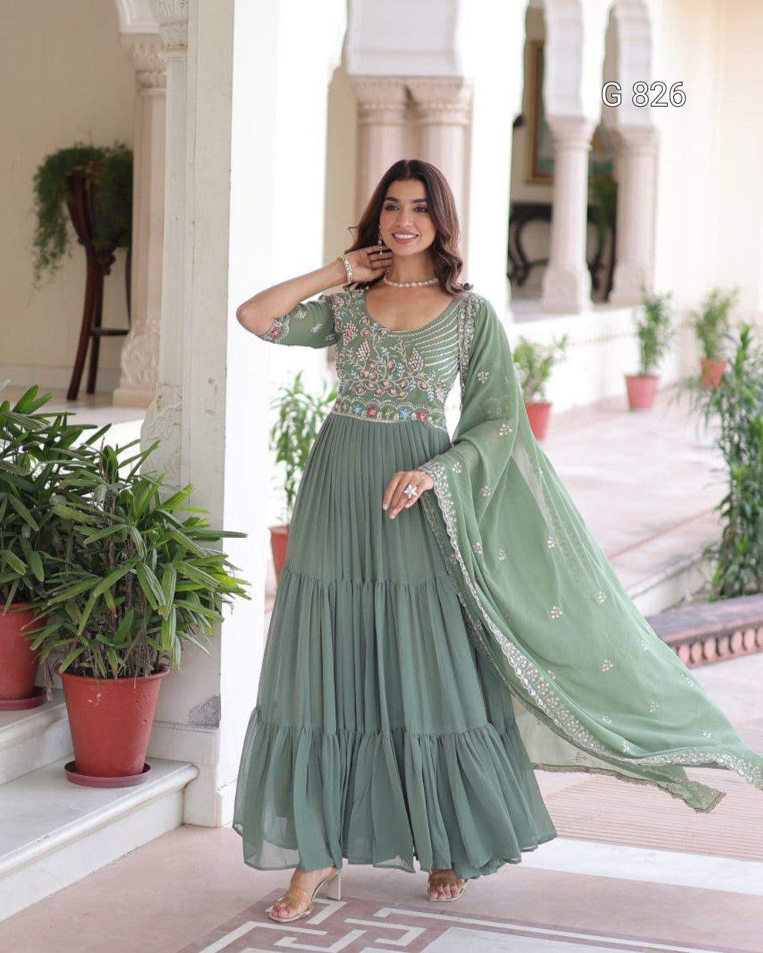 Woman in a green traditional outfit standing in an elegant indoor setting with plants.