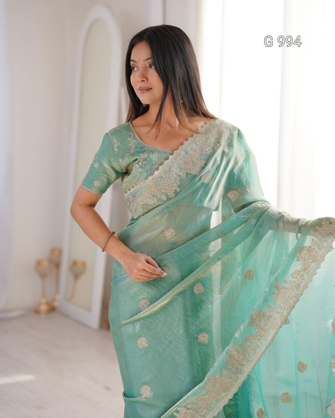 A woman modeling a mint green saree with gold floral embroidery and a matching embroidered blouse in a bright indoor setting. The text 'G 994' is visible in the top right corner.