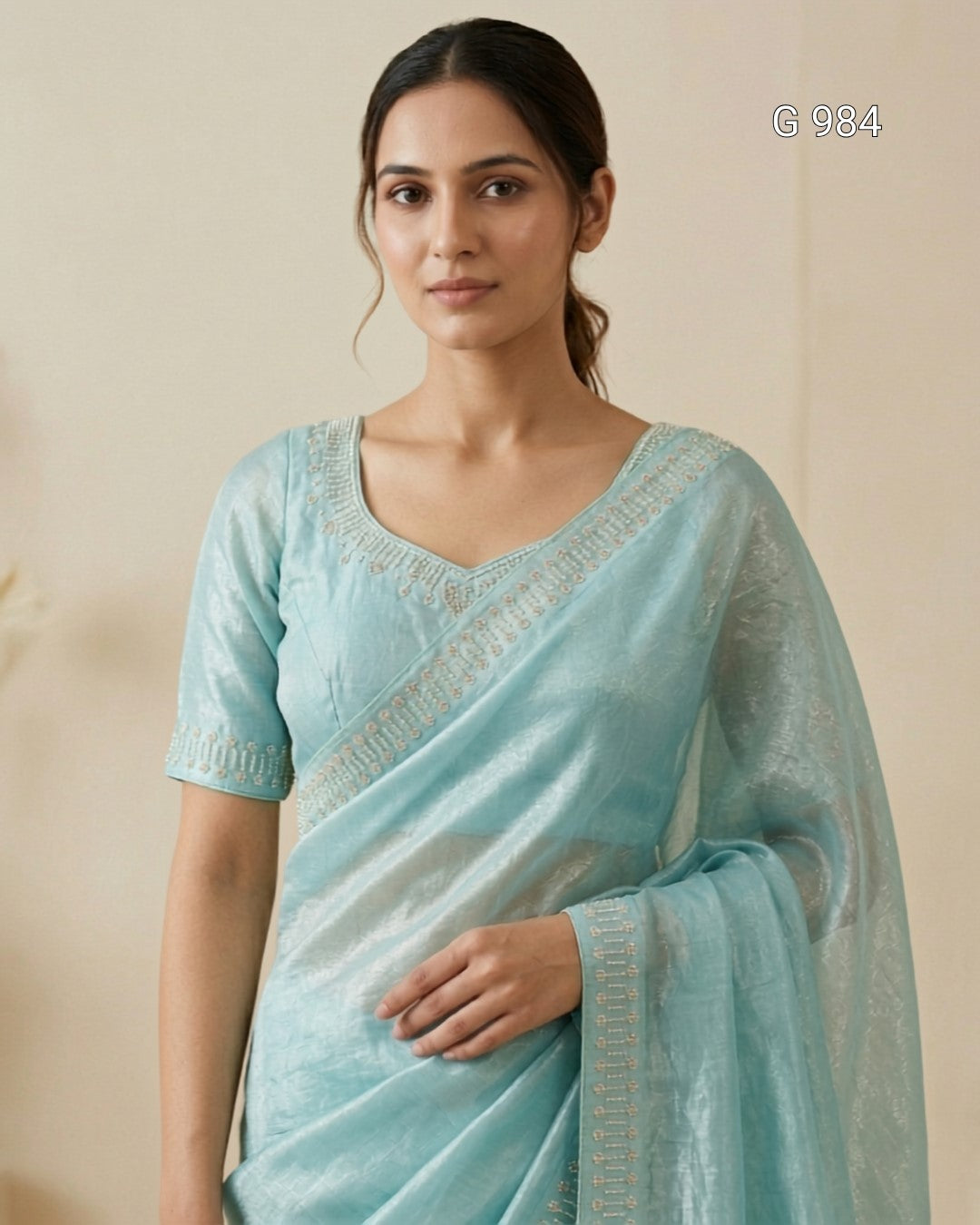 A woman wearing a light blue-green silk saree with a matching embroidered blouse, standing against a plain beige background. The text 'G 984' is visible in the top right corner.