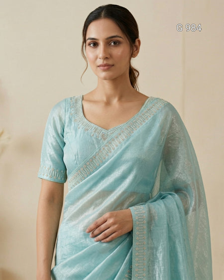 A woman wearing a light blue-green silk saree with a matching embroidered blouse, standing against a plain beige background. The text 'G 984' is visible in the top right corner.