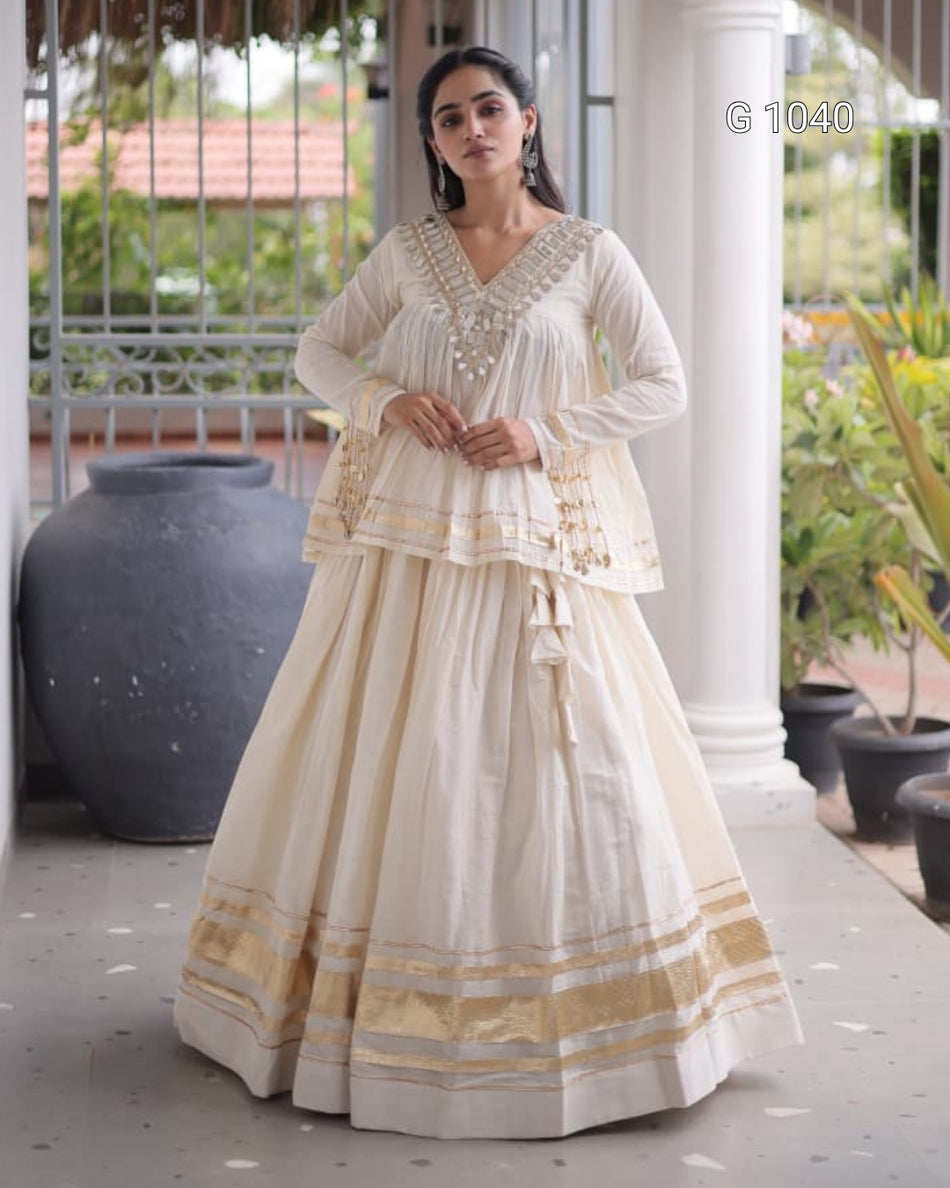 A woman modeling a traditional Indian outfit consisting of a cream-colored Anarkali kurta and a matching flared skirt with gold and silver zari borders, set in a porch environment.
