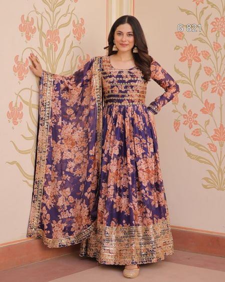 Woman wearing a floral dress with a matching dupatta against a decorative wall.