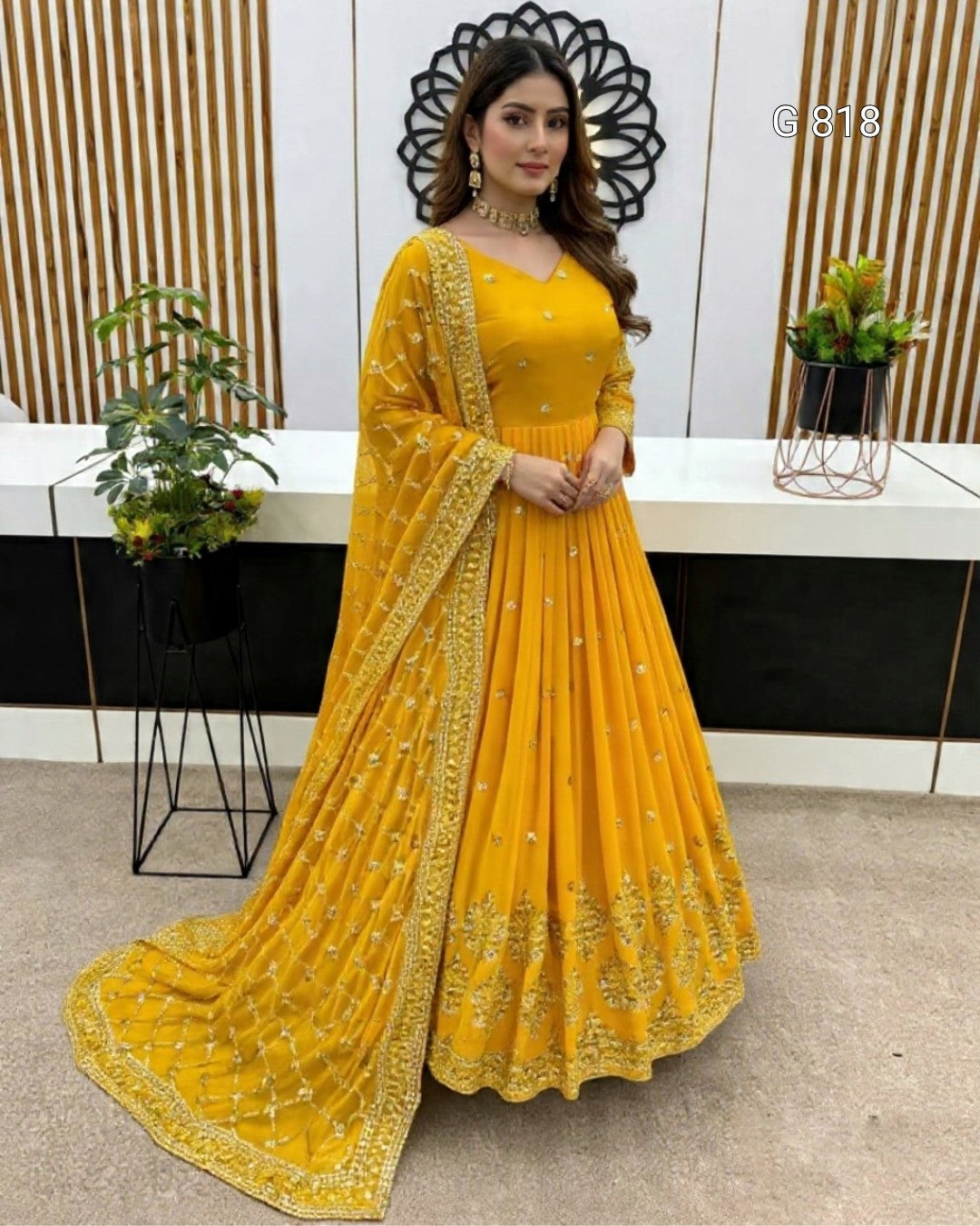 Woman in a yellow traditional outfit with intricate designs standing indoors.