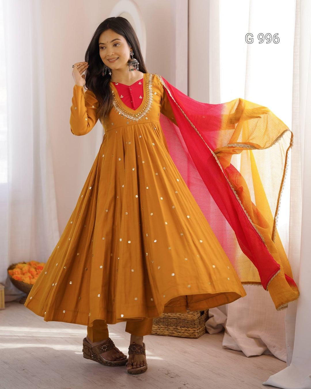 A woman models a mustard yellow Anarkali kurta with silver mirror work embroidery, paired with a red and yellow gradient dupatta, in a bright indoor setting.